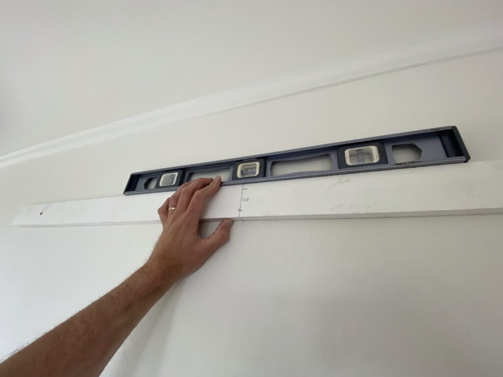 A handyman's hand holding a level on a wall in preparation for mounting a wide mirror