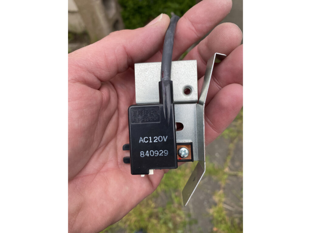 A hand holding the new igniter about to be installed to fix a tankless hot water heater