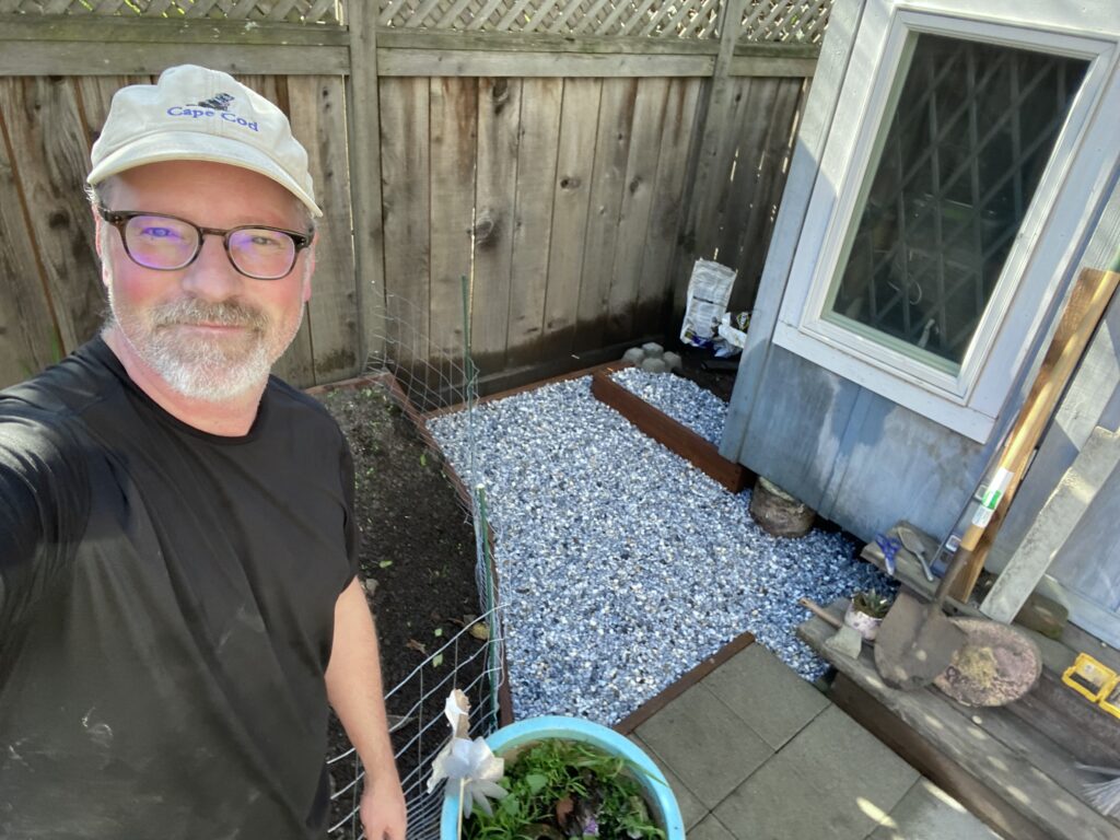 A selfie of a handyman with a newly installed gravel area behind him